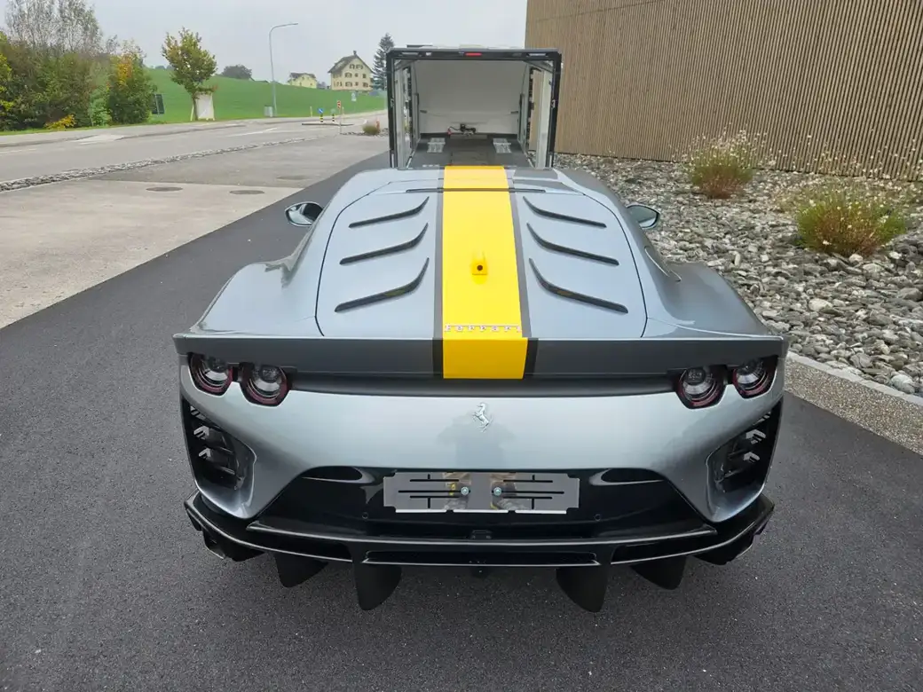 Une Ferrari grise à bande de course jaune, vue de face, garée sur une route asphaltée.