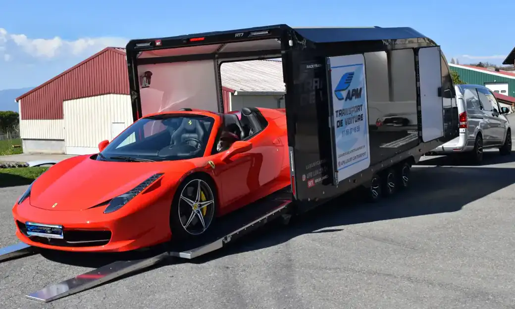 Une Ferrari décapotable rouge descend d’une rampe de camion de transport pour se garer sur un parking goudronné.