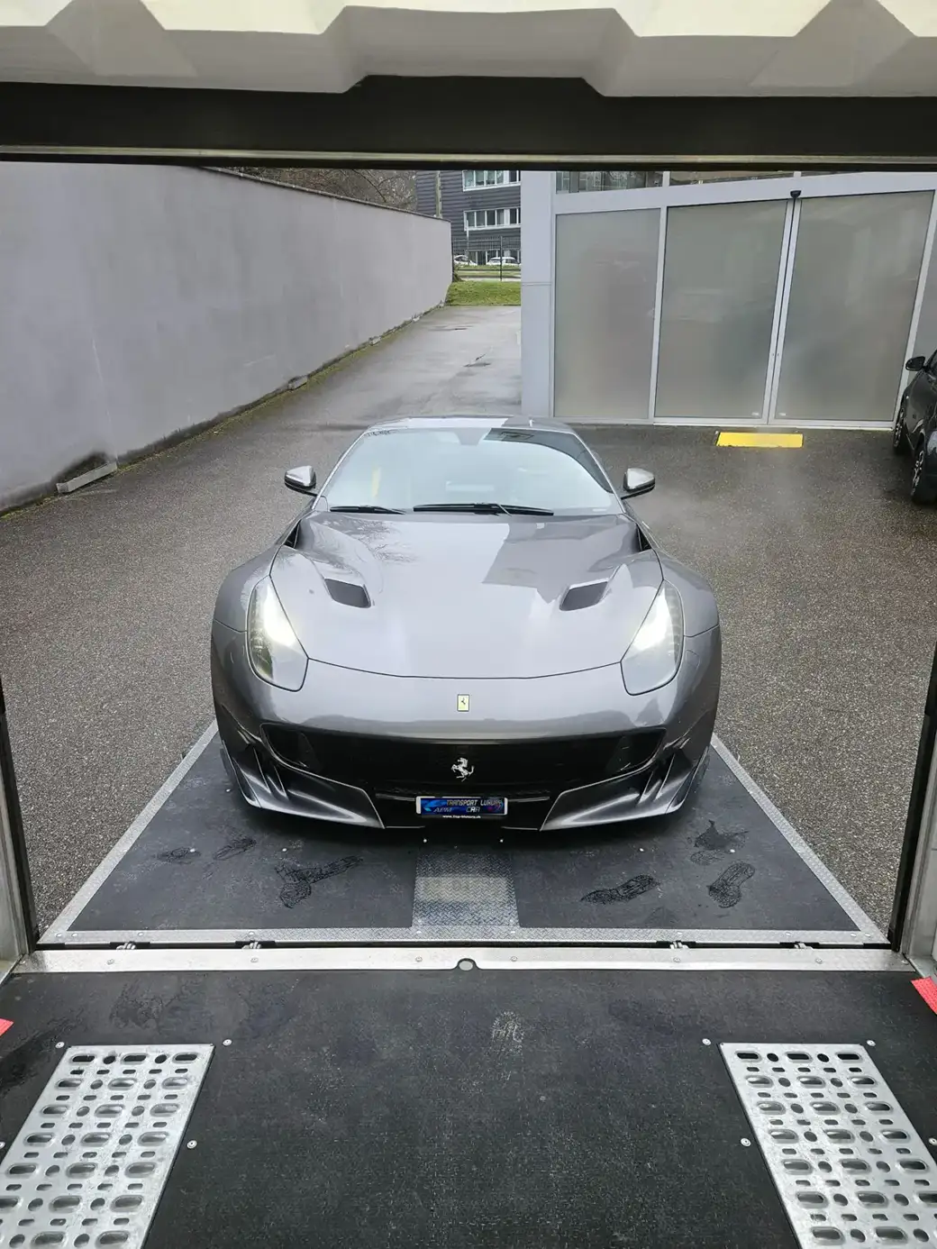 Une Ferrari gris foncé, voiture de sport, est garée sur la rampe de chargement d’une remorque de transport.