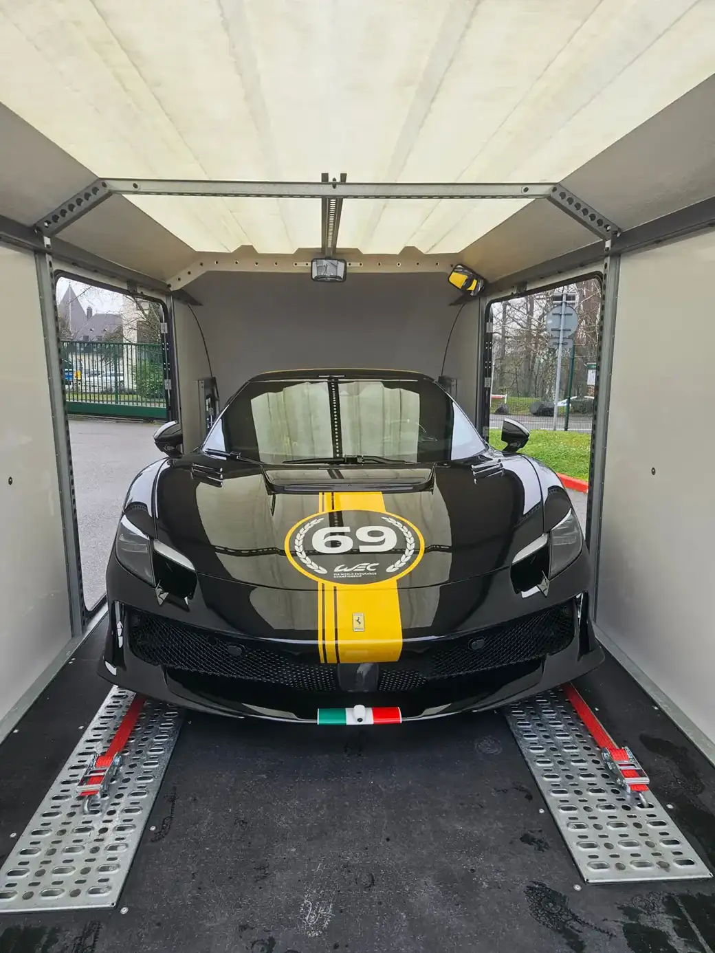 Une Ferrari noire avec une bande de course jaune et le numéro 69 dans un cercle à l’intérieur d’une remorque porte-voitures.