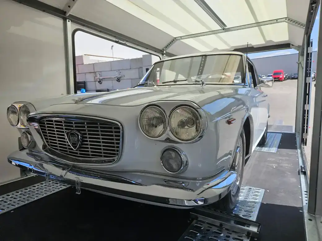 Une Lancia Flavia coupée blanche d’époque est garée à l’intérieur d’une remorque fermée.