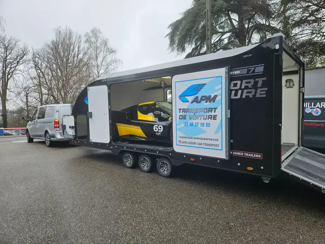 Une remorque noire le côté ouvert, révélant à l’intérieur une voiture de course jaune et noire portant le numéro 69.